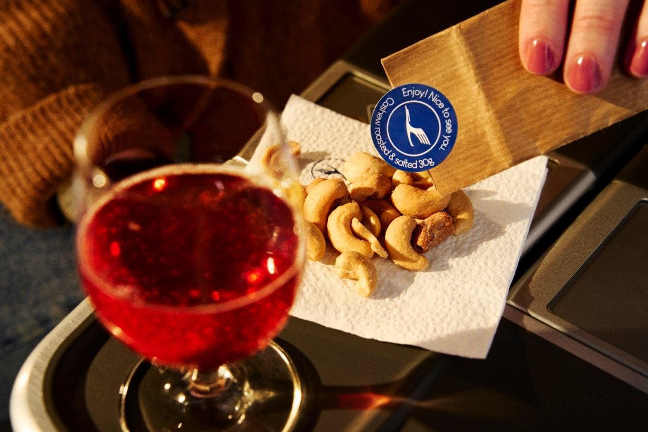 A glass of red wine and roasted cashews on a business class tray table
