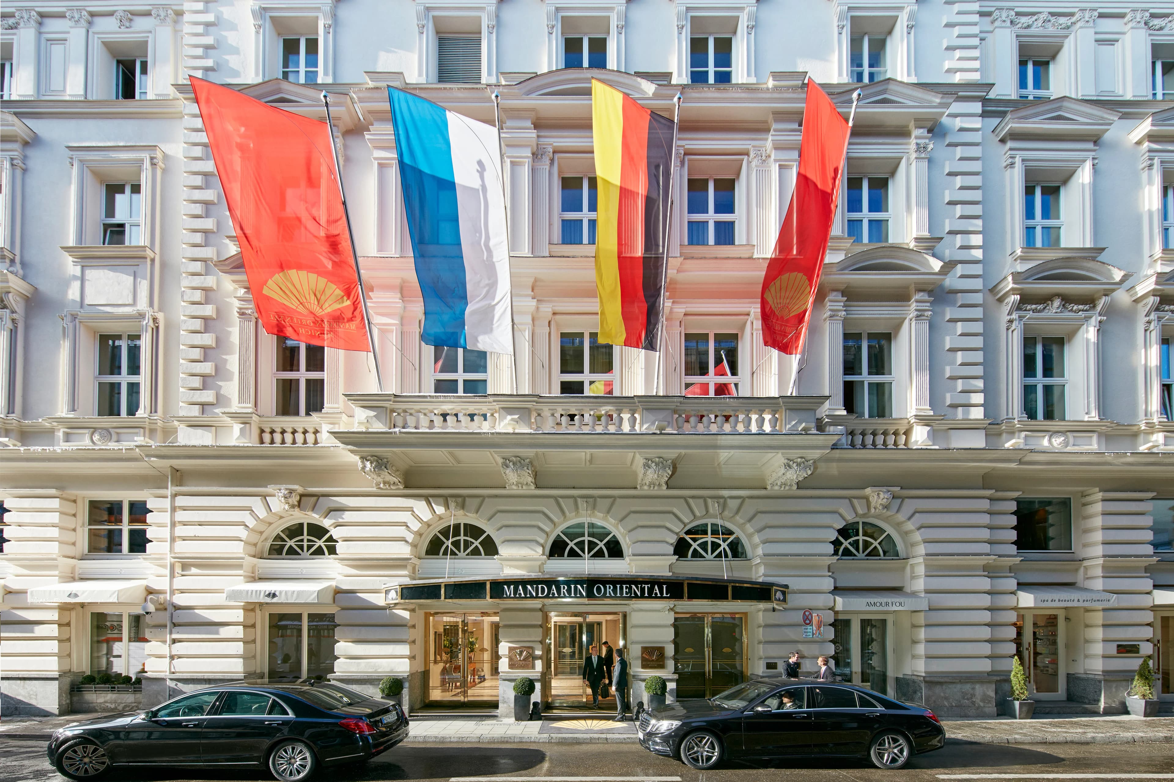 A hotel's flag-draped facade and canopied entrance on a Munich street